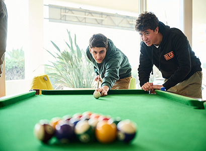 2 students playing pool, showing a close-up of the pool table and the 2 boys