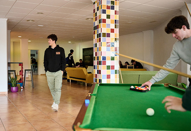 Common area of a school showing a pool table, comfortable couches, ans several students